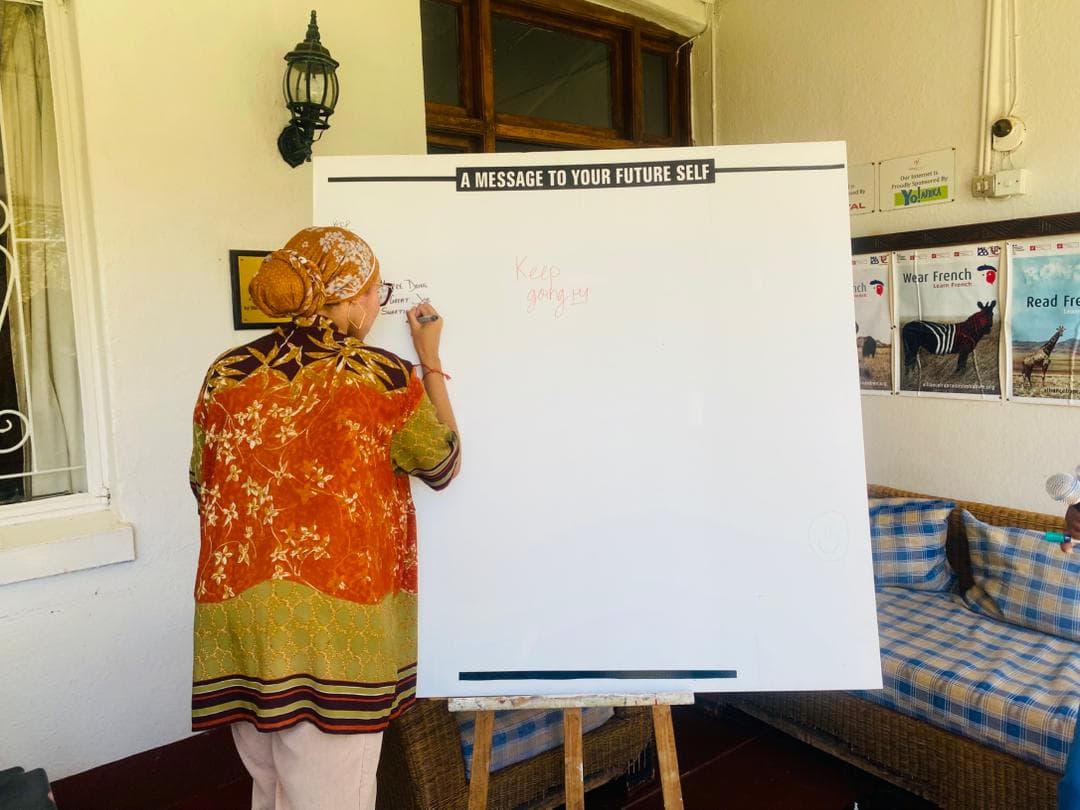 Woman writing on a large board titled 'A MESSAGE TO YOUR FUTURE SELF'.