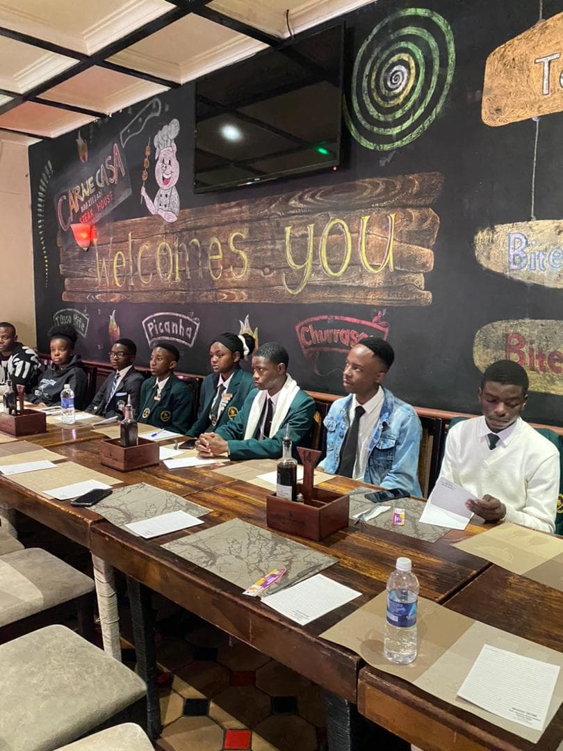 Students in uniforms sit at a long wooden table in a restaurant with chalkboard art.