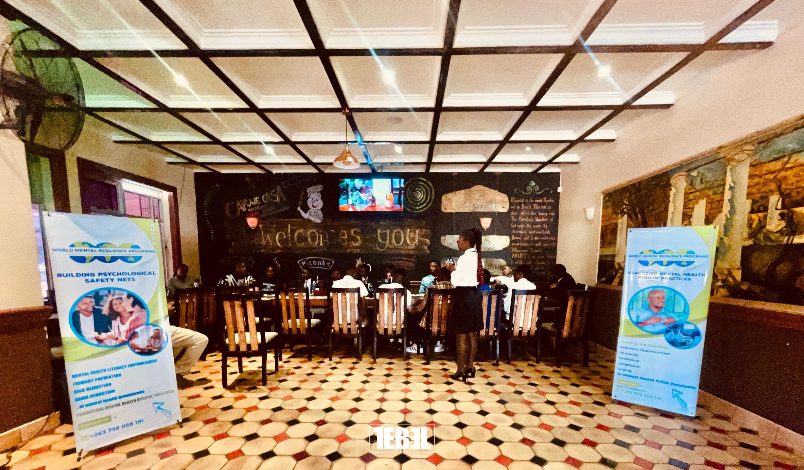 People attending a World Mental Resilience Programs event in a restaurant with large informational banners.