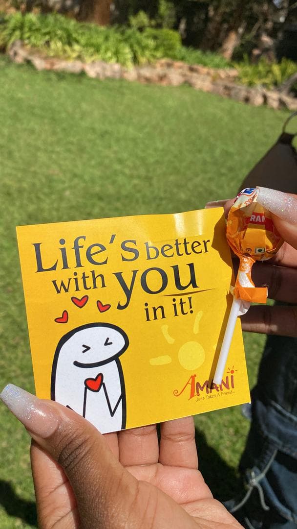 Hand holding a yellow card reading 'Life's better with you in it' and a lollipop.